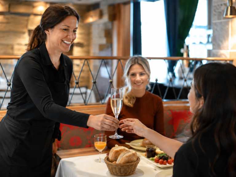 Kellnerin serviert Sekt an zwei Gäste im Restaurant