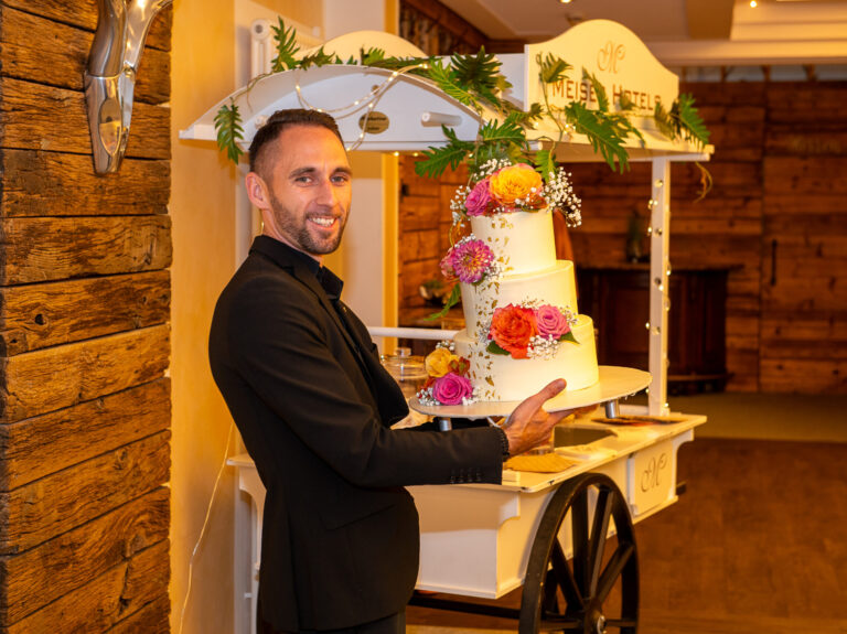 Mann präsentiert dreistöckige Hochzeitstorte mit Blumen