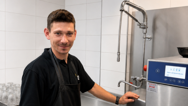 Mann bedient professionelle Spülmaschine in Großküche